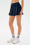 Model wears the SPLITS59 Venus High Waist Rigor Skort in Indigo, paired with white "SPL" socks and white sneakers, standing against a plain light background.