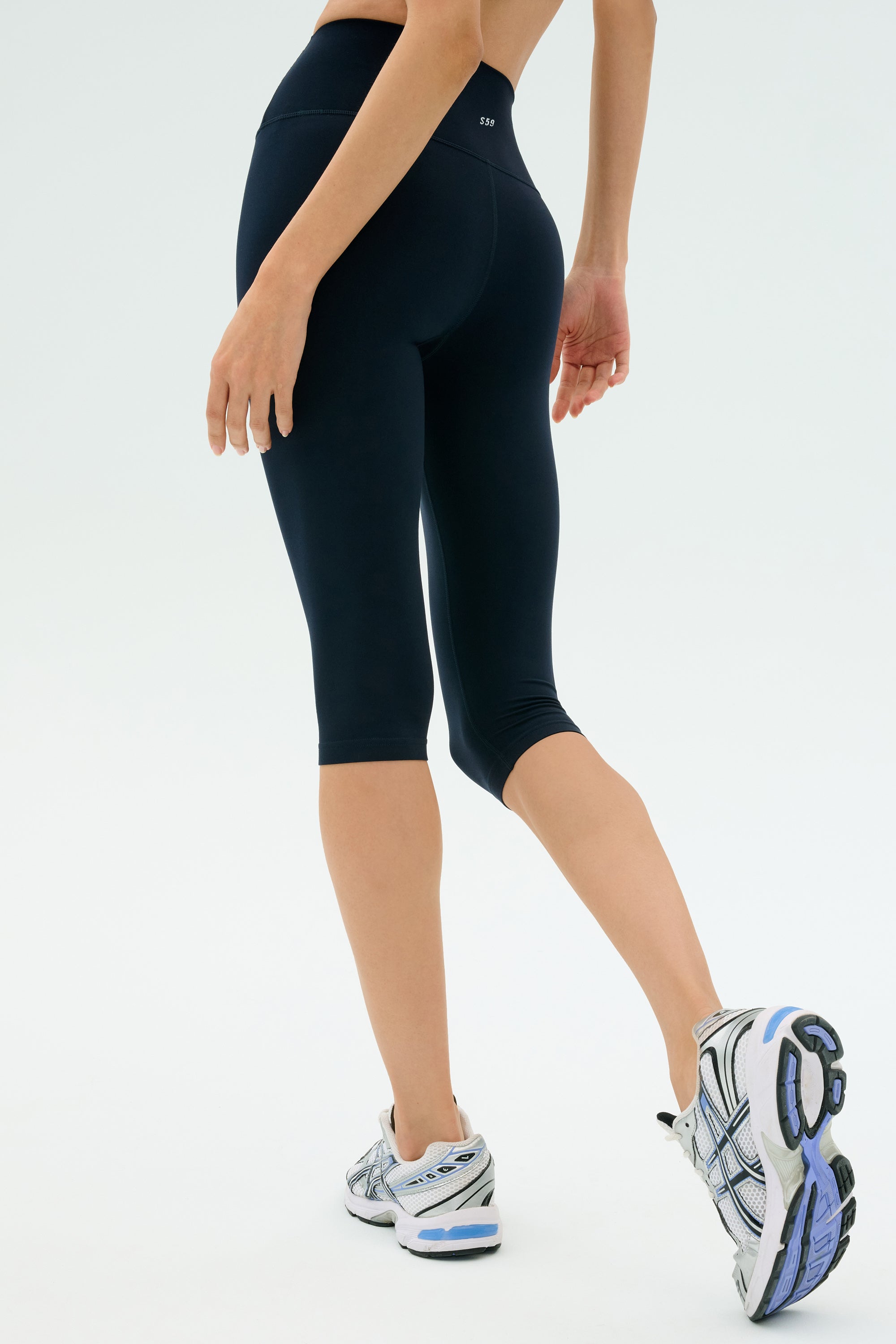 A person is photographed from behind against a plain background wearing SPLITS59 Airweight High Waist 16" Legging in indigo and white athletic shoes.