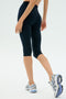 A person is photographed from behind against a plain background wearing SPLITS59 Airweight High Waist 16" Legging in indigo and white athletic shoes.