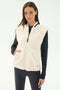 A woman stands against a plain light background wearing the SPLITS59 Aster Sherpa Vest - Creme over a black long-sleeve top and leggings—an ideal warm layer for cool weather workouts.