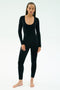 A person stands barefoot against a plain background, wearing the SPLITS59 Chloe Airweight Jumpsuit in black—a fitted, long-sleeve one piece with a scoop neckline crafted from soft Airweight fabric.