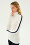 A person with long blonde hair is wearing a white SPLITS59 Jackson Rib Full Length Turtleneck in White/Indigo, featuring a black stripe along the sleeves, and is posing against a plain background.
