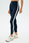 A person in SPLITS59's Layla Airweight High Waist 7/8 leggings in Indigo/White side stripe with white New Balance sneakers stands on a white background.