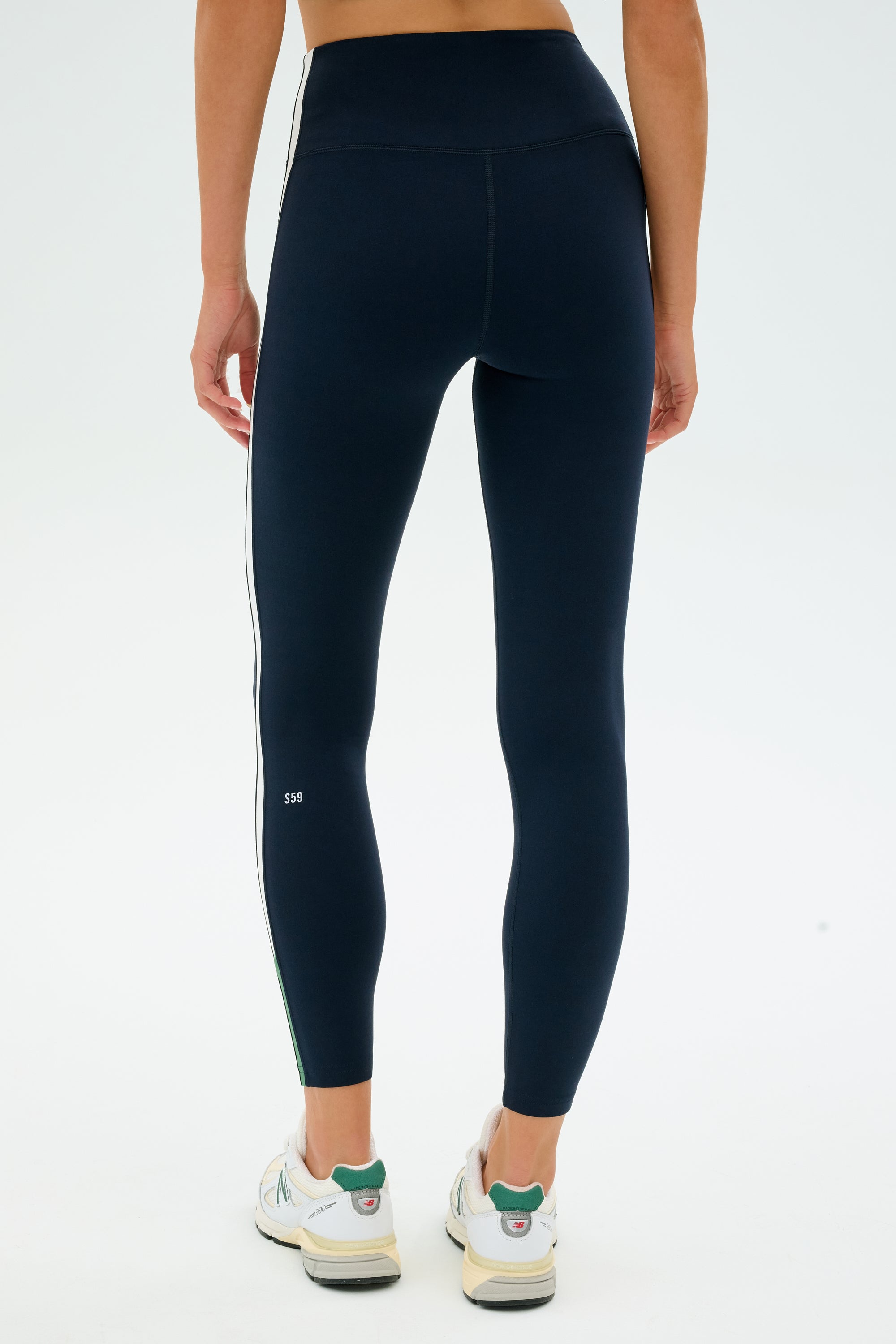 Someone in SPLITS59's Layla Airweight High Waist 7/8 leggings in Indigo/White and white sneakers, facing away from the camera on a plain white backdrop.