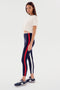 A woman in a Djuna Crop Ringer - White/Indigo by SPLITS59 and leggings with red and white stripes stands posing sideways. She is also wearing black sneakers, perfect for warm weather workouts.