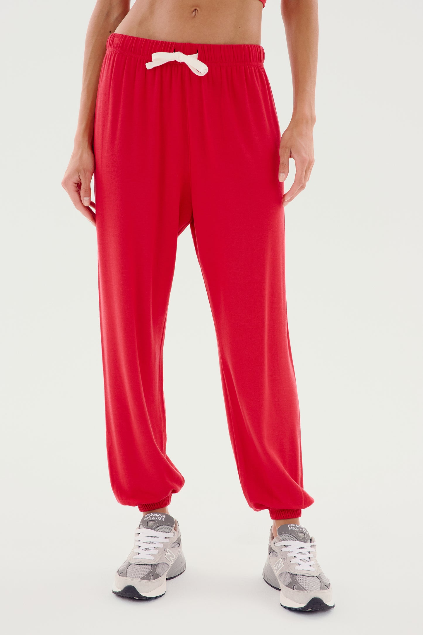 Person standing against a white background, wearing red Andie Oversized Fleece Sweatpant - Pirate Red by SPLITS59 with a white drawstring and grey athletic shoes. The person's head is not visible in the image.