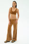 A woman stands against a plain background wearing the SPLITS59 Joy Velour Pant in Honey, a brown polyester spandex sports bra, and multicolored sneakers.