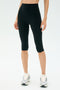 A person wears SPLITS59 Airweight High Waist 16" Legging in black with white running shoes, standing against a plain light background.