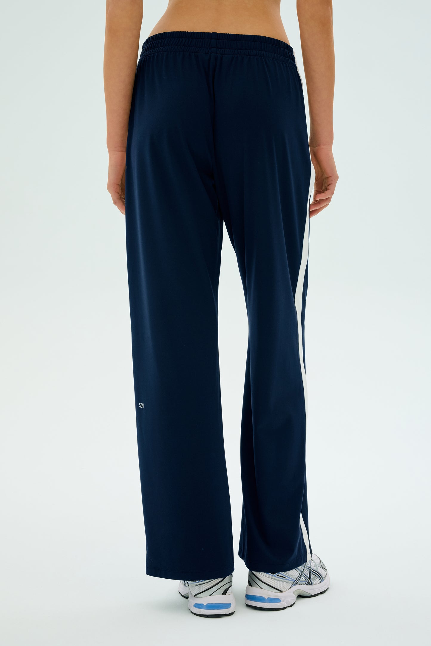 The person is wearing SPLITS59's Maxie Rigor Track Pant in indigo and white, featuring a wide-leg silhouette paired stylishly with crisp white sneakers.