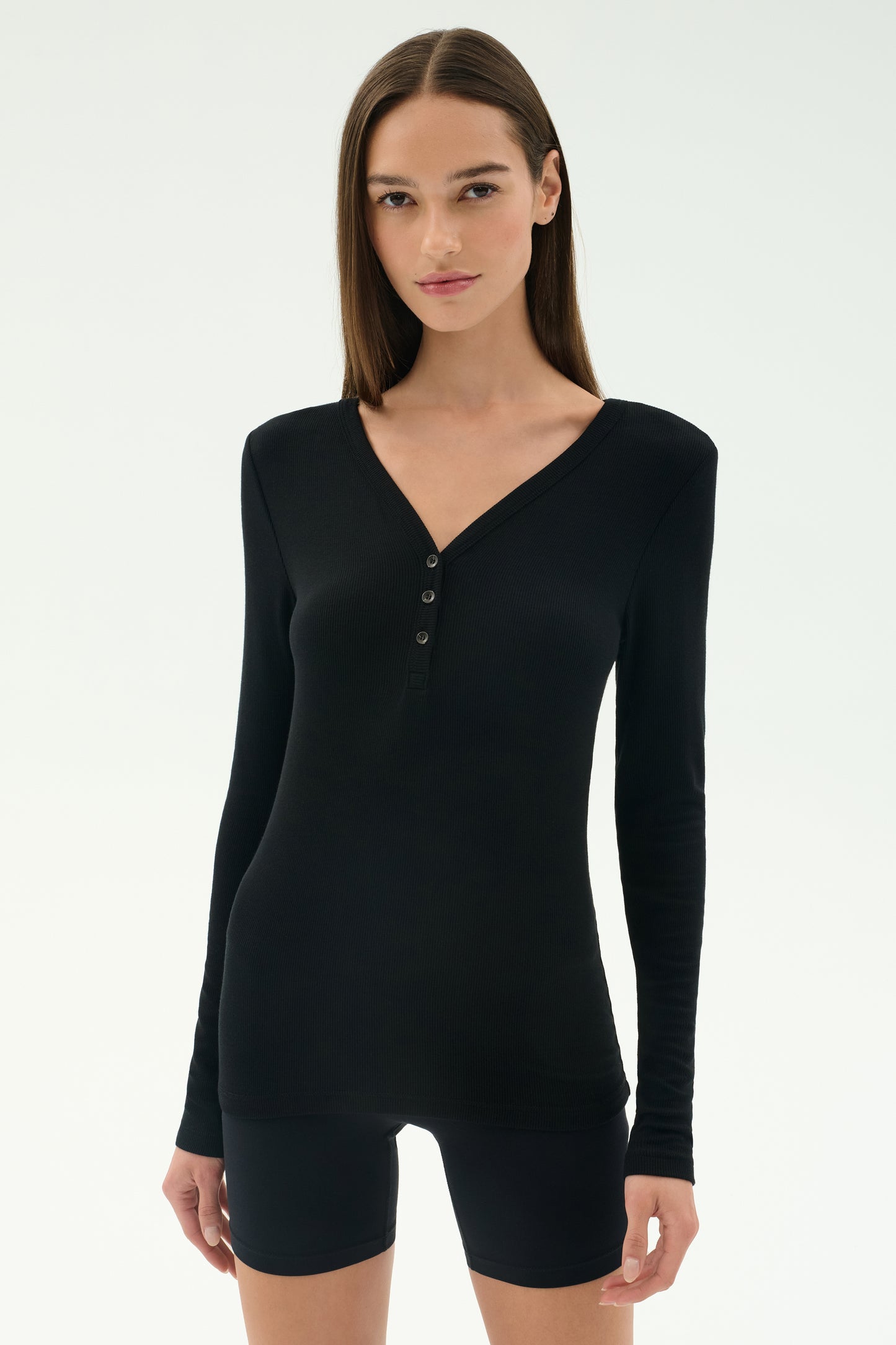 A woman faces forward against a plain light background, wearing the SPLITS59 Louise Rib Henley in black with black shorts.