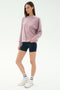 A woman stands against a plain background wearing the SPLITS59 Joy Velour Crewneck in Blush, navy spandex bike shorts, white socks, and white sneakers.