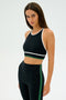 A model showcases the SPLITS59 Layla Airweight Bra in Black/Arugula, standing against a plain white background.