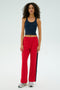 A curly-haired individual in a navy tank top and SPLITS59 Maxie Rigor Track Pant in Pirate Red/Indigo with a wide-leg silhouette, paired with sneakers, stands against a plain backdrop.