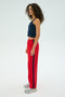 A person with curly hair in a navy tank top and SPLITS59's Maxie Rigor Track Pant in Pirate Red/Indigo stands sideways in silver sneakers against a plain background.