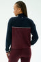A person with braided hair is shown from the back wearing the SPLITS59 Millie Airweight Half Zip in Dark Cherry/Indigo, standing against a plain light background.