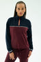 A woman wears the SPLITS59 Millie Airweight Half Zip in Dark Cherry/Indigo with matching pants, made from a nylon-spandex blend, standing against a plain light background.