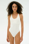 A person with curly hair wears the SPLITS59 Suki Airweight Bodysuit in white, made from soft spandex, standing against a plain light background.