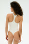 A person with curly hair stands facing away, wearing the SPLITS59 Suki Airweight Bodysuit in white, made from smooth nylon-spandex fabric, set against a plain light background.