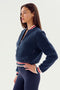 A person stands in profile wearing the SPLITS59 Willa Sherpa Jacket - Indigo with a zipper and striped cuffs, perfect for cozy winter workouts, over navy blue leggings.