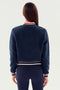 Rear view of a person with long, straight brown hair wearing a navy blue, cozy SPLITS59 Willa Sherpa Jacket - Indigo with striped cuffs and hem, paired with dark pants against a plain white background.