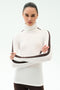 A woman stands with arms crossed, wearing the SPLITS59 Jackson Rib Full Length Turtleneck in White/Dark Chocolate—ideal for yoga or running—against a plain light background.