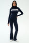 A woman wears the SPLITS59 Lennon Rib Turtleneck in Indigo/White with navy flared pants and white sneakers, standing against a plain light background.