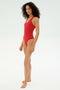 A person stands barefoot wearing the SPLITS59 Suki Airweight Bodysuit in Pirate Red against a plain white background.