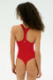 A woman with curly hair models the SPLITS59 Suki Airweight Bodysuit in Pirate Red, a stretchy one-piece shown from the back against a plain light background.