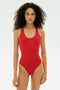 A woman with curly hair faces forward, wearing the SPLITS59 Suki Airweight Bodysuit in Pirate Red, made of nylon and spandex, against a plain white background.