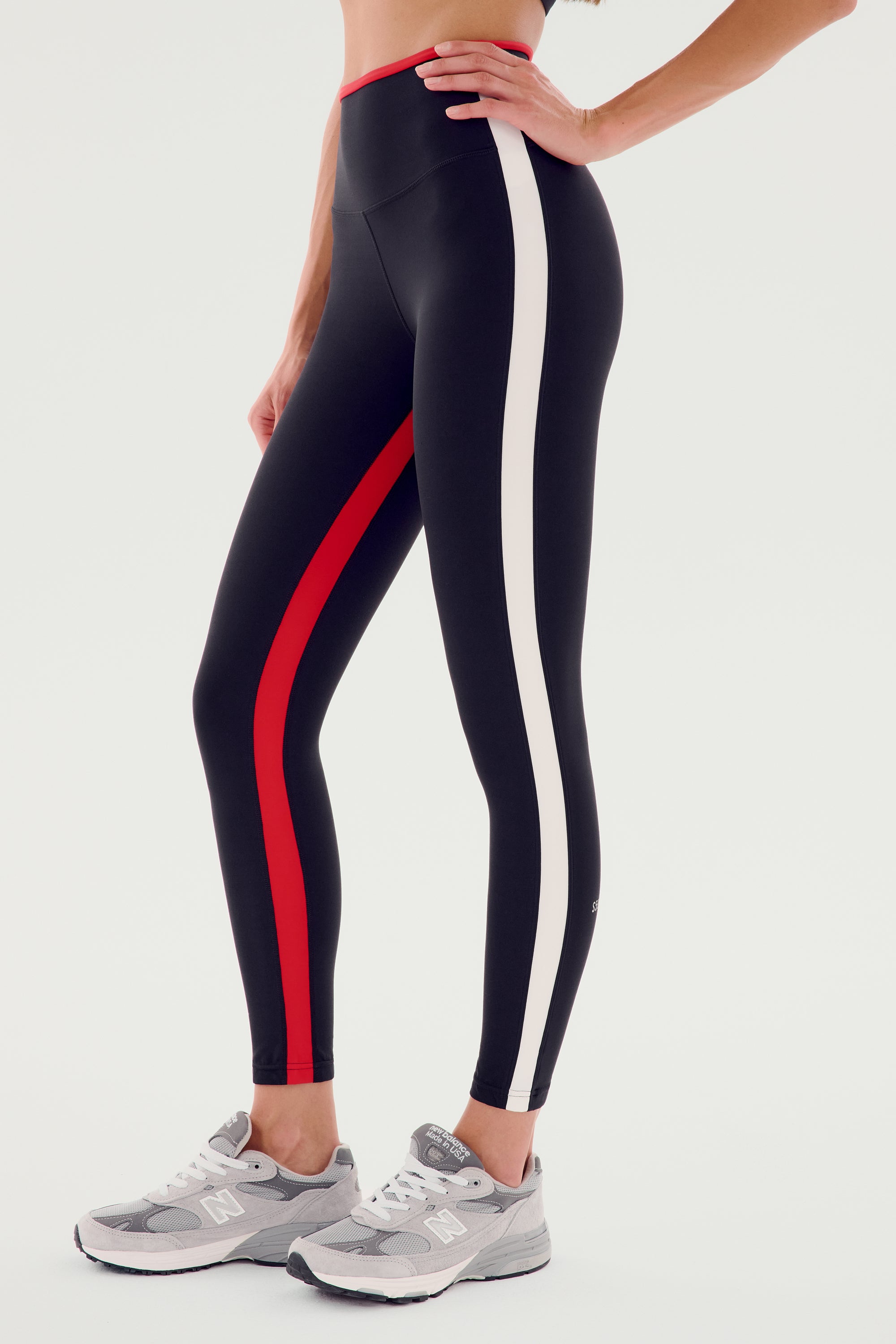 A person is wearing SPLITS59 Sam High Waist Rigor 7/8 - Black/Pirate Red, perfect for yoga, along with gray athletic shoes against a white background.