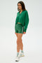 A person is wearing the Joan Fleece Polo Sweatshirt in Arugula by SPLITS59, paired with striped shorts, white sneakers, and socks against a plain background.