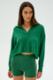 A person in a green SPLITS59 Joan Fleece Polo Sweatshirt and green biker shorts looks sideways against a plain background.