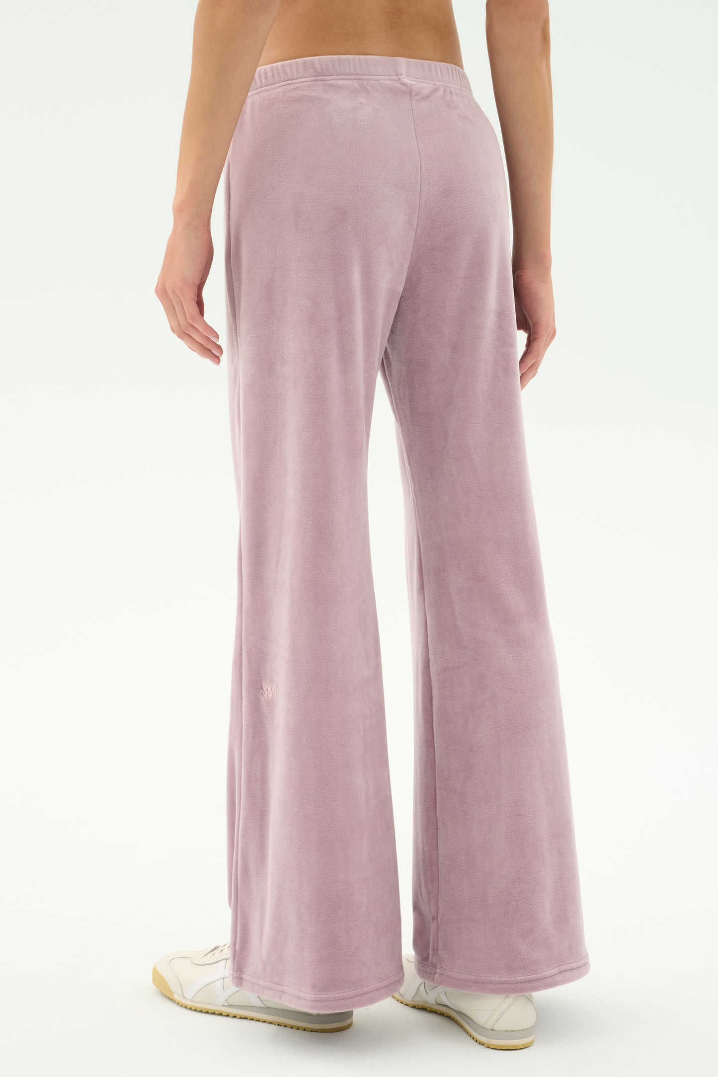 Person wearing SPLITS59 Joy Velour Pant in Blush and white sneakers, shown from the back against a plain light background.