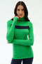 A woman wears the SPLITS59 Lennon Rib Turtleneck in Grass/Indigo, featuring a green ribbed design with a horizontal navy stripe, standing against a plain light background.