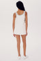 A person with long braids stands facing away, wearing the SPLITS59 Martina Rigor Dress w/Piping - White paired with white sneakers, against a plain background.