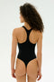 A person with curly hair is shown from the back, wearing the SPLITS59 Suki Airweight Bodysuit in black, ideal for Pilates, against a simple light background.