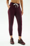 A person models SPLITS59's Reena Fleece 7/8 Sweatpant in Dark Cherry, featuring soft modal with spandex stretch, styled with matching sneakers and a white drawstring, hands in pockets against a plain background.