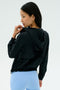 A woman wearing the SPLITS59 Megan Woven Nylon Jacket in black stands facing away, looking over her shoulder against a plain light background.