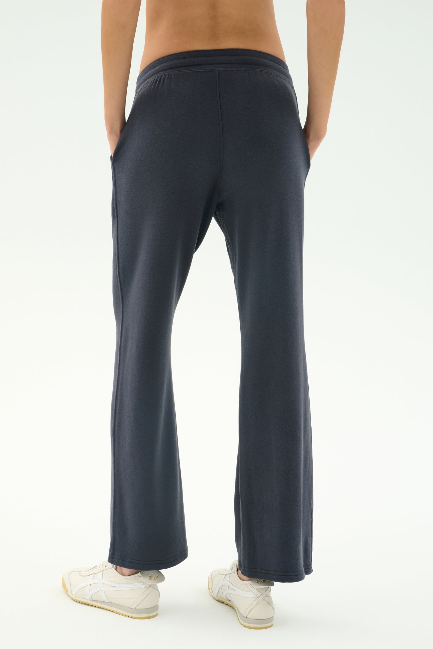 A person stands with their back to the camera, hands in pockets, wearing SPLITS59 Raven Fleece Full Length Sweatpant in Graphite and white sneakers, set against a plain light background.
