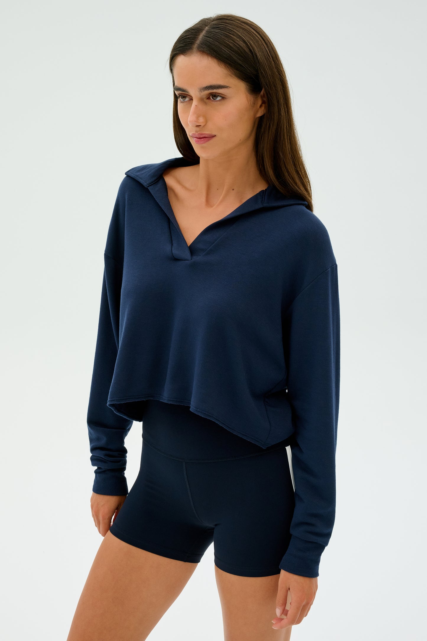 A person with long brown hair is wearing a SPLITS59 Joan Fleece Polo Sweatshirt in Indigo and navy blue shorts, crafted from soft modal fabric, set against a plain white background.