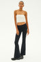 A person stands against a plain background, wearing the SPLITS59 Hazel Airweight Crop Bandeau in white paired with black flared pants made from stretch fabric and completing the look with black sneakers.