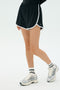 A person wears the SPLITS59 Megan Woven Nylon Run Short in Black with white trim, white socks, and silver running shoes, standing against a plain light background.