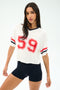 A woman poses against a plain backdrop wearing the SPLITS59 Rex Varsity Jersey V-Neck in white/59 and black athletic shorts made from a comfy elastane blend.