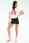 A woman poses in the SPLITS59 Rex Varsity Jersey V-Neck - White/59, made from a soft viscose/elastane blend, styled with black shorts, striped socks, and white sneakers against a plain background.