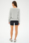 A person wearing a versatile pullover, SPLITS59's Bennie Fleece V-Neck Sweatshirt in Heather Grey/White, black shorts, and sneakers is standing and facing away.
