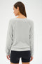 A woman in a SPLITS59 Bennie Fleece V-Neck Sweatshirt in Heather Grey/White and black shorts stands facing away, with her head slightly turned to the left.