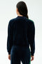 A person with long dark hair, seen from behind, wears the SPLITS59 Heritage Velour Bomber in Indigo/Grass—ideal for yoga—against a plain light background.
