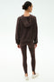 A person stands facing away, wearing the SPLITS59 Joey Long Sleeve Hoodie in Dark Chocolate, brown leggings, and white sneakers against a plain light background.