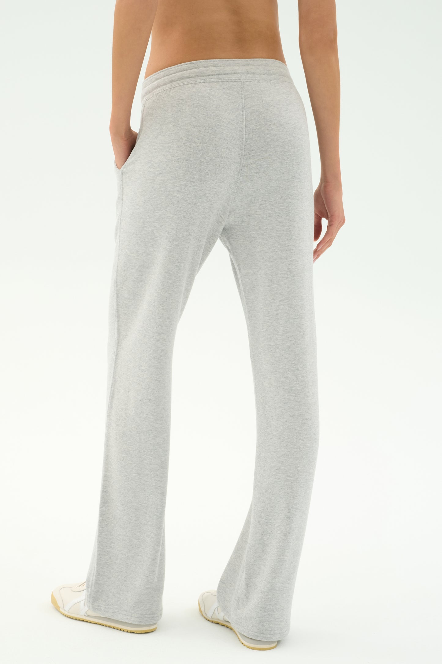 Person standing with their back to the camera, wearing SPLITS59 Raven Fleece Full Length Sweatpant in Heather Grey and white shoes against a plain white background.
