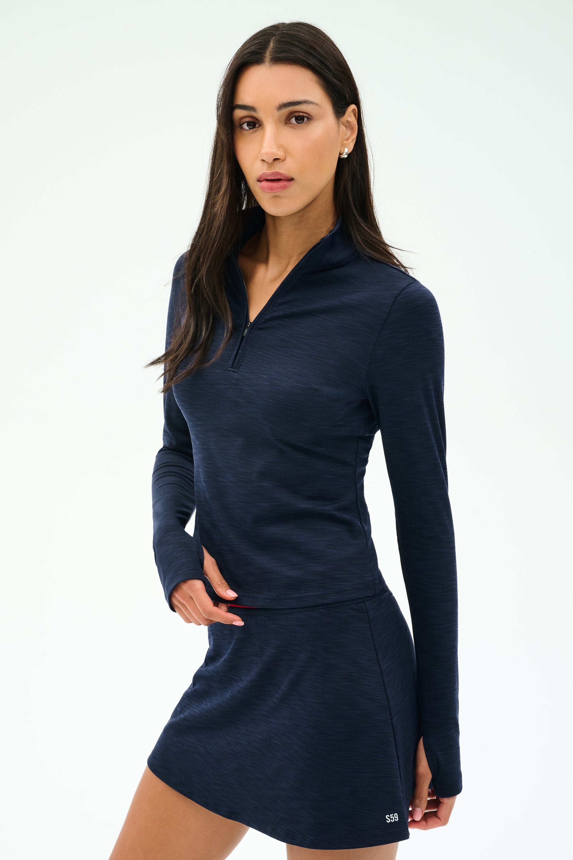 A woman wears the SPLITS59 Stevie Active Rib Half Zip Waist Length in Heather Indigo, standing against a plain light background and looking at the camera.